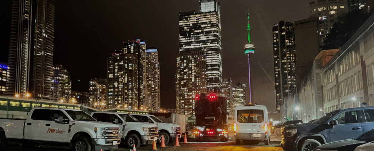 An image showing the city at night and some Toronto Terminals Railway trucks in a parking lot