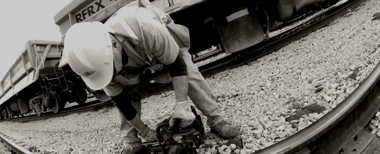 A TTR worker in black and white bent down holding a tool