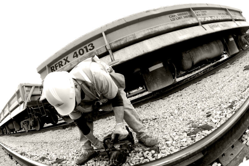 A black and white image of a TTR worker bent over with a tool working on the tracks