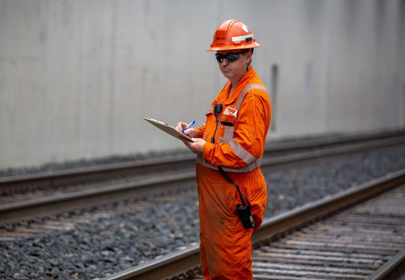 Image of TTR worker with a clipboard standing beside the tracks